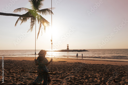 Woman traveller is siting on a swing and enjoy looking beautiful sunset with backgound of Nang Thong Beach in Khao lak lighthouse at Phang Nga Province, Thailand.  photo
