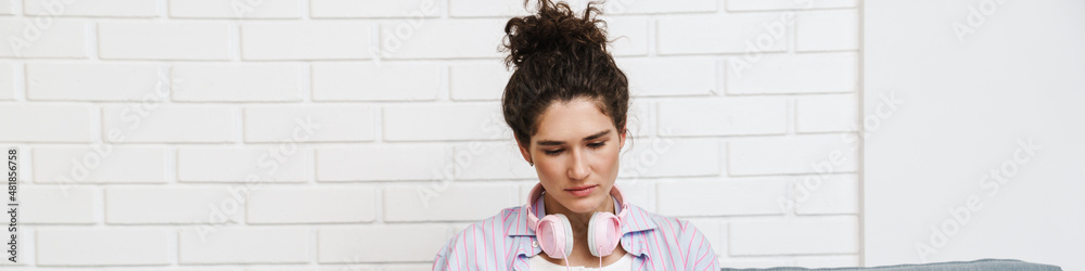 The curly-haired woman with headphones on her neck sitting on the sofa and looking at a magazine in a room The curly-haired woman with headphones on her neck sitting on the sofa and looking at a magazine in a room