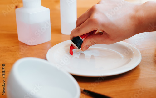 Close-up of female artist's hand squeezing out red paint for painting from tube. Selective soft focus