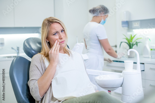 Caucasian woman suffering from terrible toothache at a dental clinic. Dentist preparing for the examination of her female client with painful cavities.