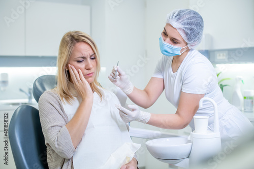 Middle shot of a Caucasian woman with a toothache sitting in the dental chair while a female dentist trying to examine her.