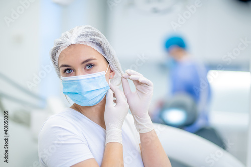 Konstfotografi Portrait of a Caucasian young female doctor or nurse wearing a protective face mask, and protective gloves, putting on a white surgical cap