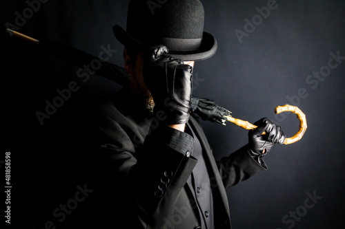 Portrait of Man in Dark Suit Holding Umbrella and Doffing Bowler Hat. Vintage Style and Retro Fashion of Classic English Gentleman.