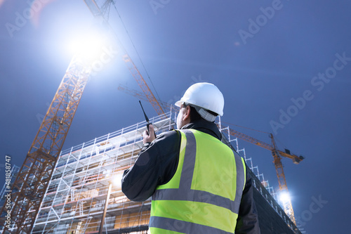 architect engineer worker with hard hat on construction site at night shift communicating with two way radio 