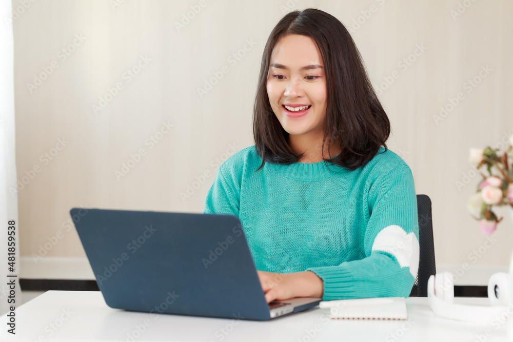 Candid young smiley Asian woman sitting at desk working online on her laptop computer. Businesswoman typing on computer at workplace Woman working in home office Candid young smiley Asian woman sitting at desk working online on her laptop computer. Businesswoman typing on computer at workplace Woman working in home office