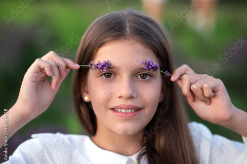 beautiful young girl with long hair outdoors with summer flowers. Cheerful Little girl holding lavender flowers on field. Close up portrait smiling girl with big eyes. Provence