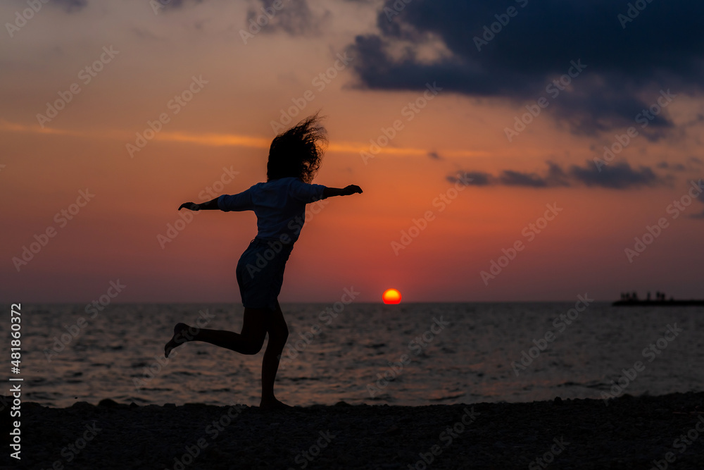 Happy young woman having fun with open hands at the sunset on sea.