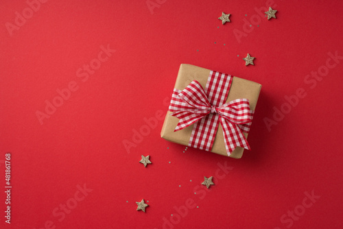 Top view photo of valentine's day decorations craft paper giftbox with checkered ribbon bow sequins and stars on isolated red background with empty space © ActionGP