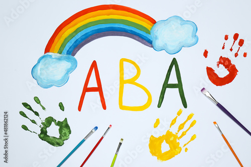 Drawn abbreviation ABA (Applied behavior analysis), rainbow, palm prints and paintbrushes on white paper, flat lay photo