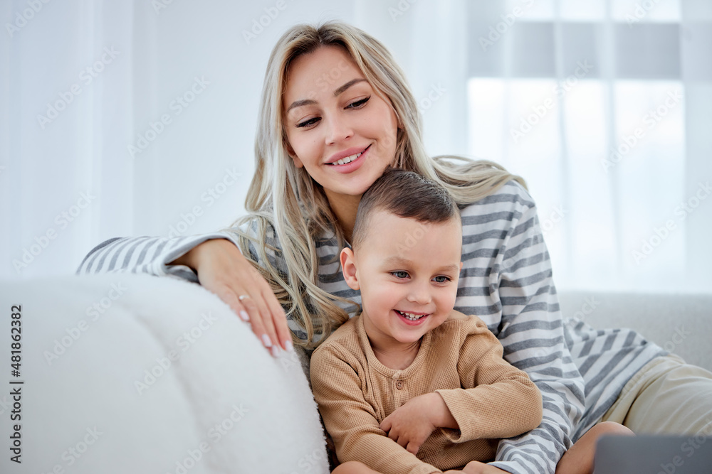 smiling young mother with little kid sit on sofa in living room have fun using modern laptop together, smiling parent rest on sofa enjoy weekend with small child, watch video cartoon on computer smiling young mother with little kid sit on sofa in living room have fun using modern laptop together, smiling parent rest on sofa enjoy weekend with small child, watch video cartoon on computer