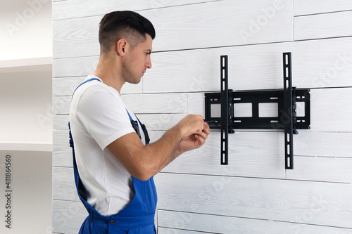 Professional technician with screwdriver installing TV bracket on wall indoors photo