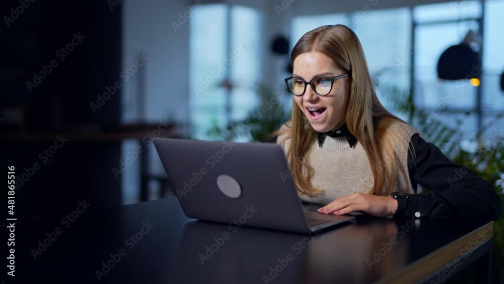 Female employee opens laptop and exclaims in surprise. Happy young woman cheering, smiling and gesturing in excitement. Blurred background.