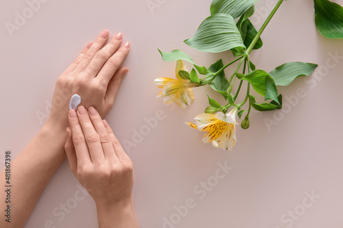 Female hands with cosmetic cream and flowers on light background