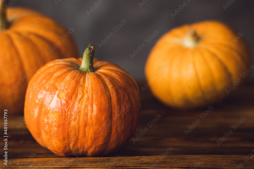 Three orange pumpkins on the brown table and grey background. Selective focus. Three orange pumpkins on the brown table and grey background. Selective focus.