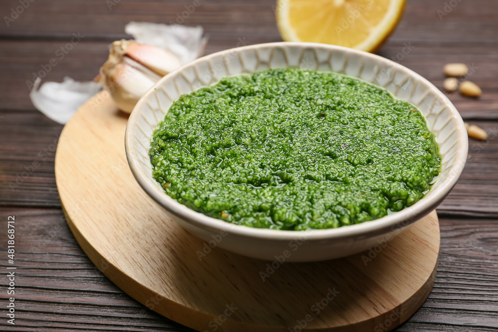 Bowl of tasty pesto sauce and ingredients on wooden background Bowl of tasty pesto sauce and ingredients on wooden background