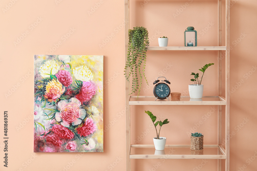 Fototapeta premium Wooden shelving unit with plants, alarm clock and painting hanging on pink wall