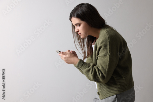 Young woman with bad posture using smartphone on grey background. Space for text