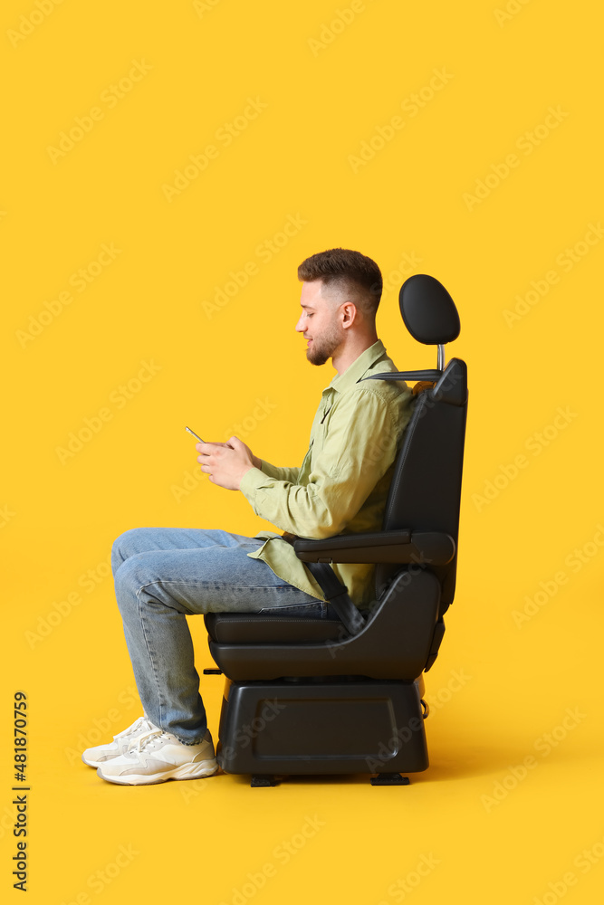 Young man in car seat and with phone on color background
