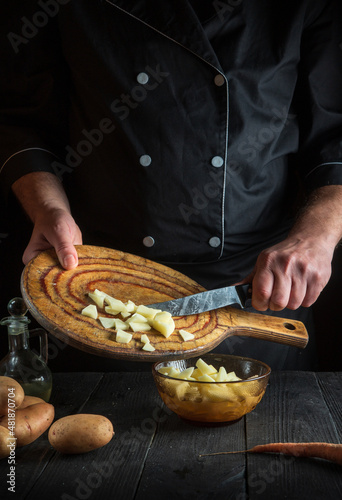 Professional chef prepares raw potatoes for lunch or dinner. Close-up of a cook hands while working in restaurant kitchen