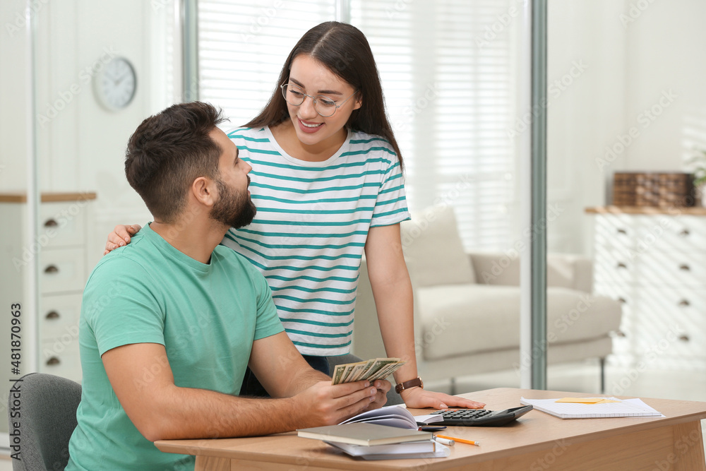 Happy young couple counting money at wooden table indoors Happy young couple counting money at wooden table indoors