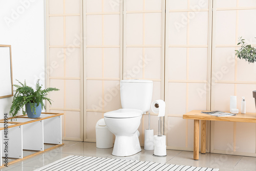 Interior of restroom with toilet bowl, paper holder and furniture with houseplants photo