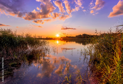 Beautiful scenic view at nice landscape on a beautiful lake and colorful sunset with reflection on water with green gras on foreground and glow on a background, spring season landscape
