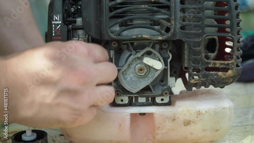 repair of a lawn mower. the man puts down the phone from the gas tank. he is sorting through the mower