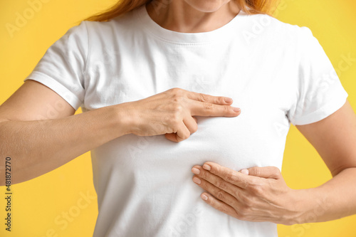 Mature woman feeling discomfort in her breast on color background. Cancer awareness concept