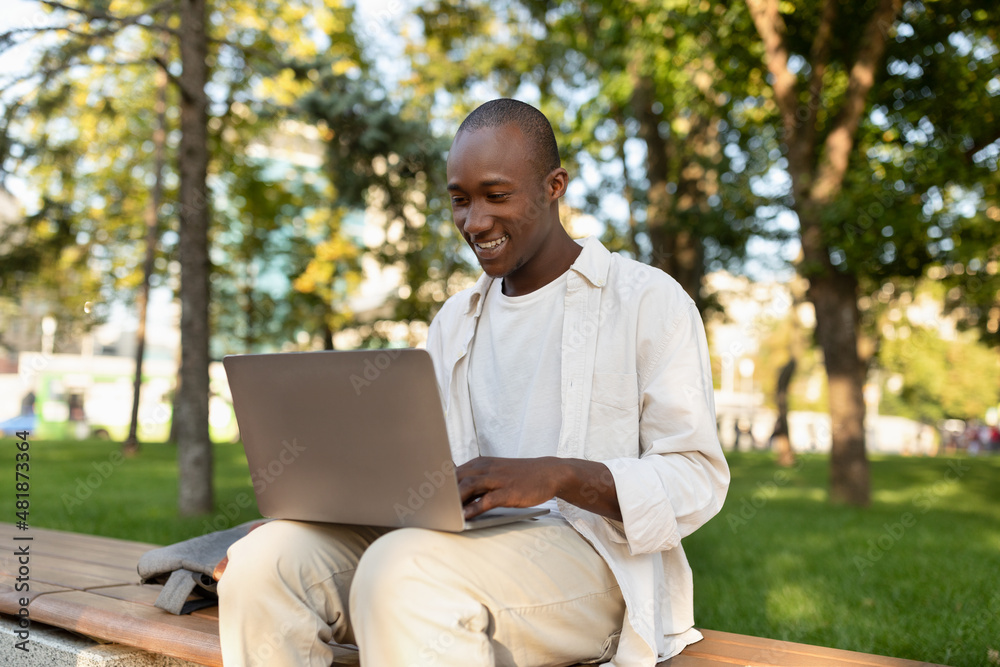 African american male student using laptop and learning online, doing homework outdoors in university campus park African american male student using laptop and learning online, doing homework outdoors in university campus park