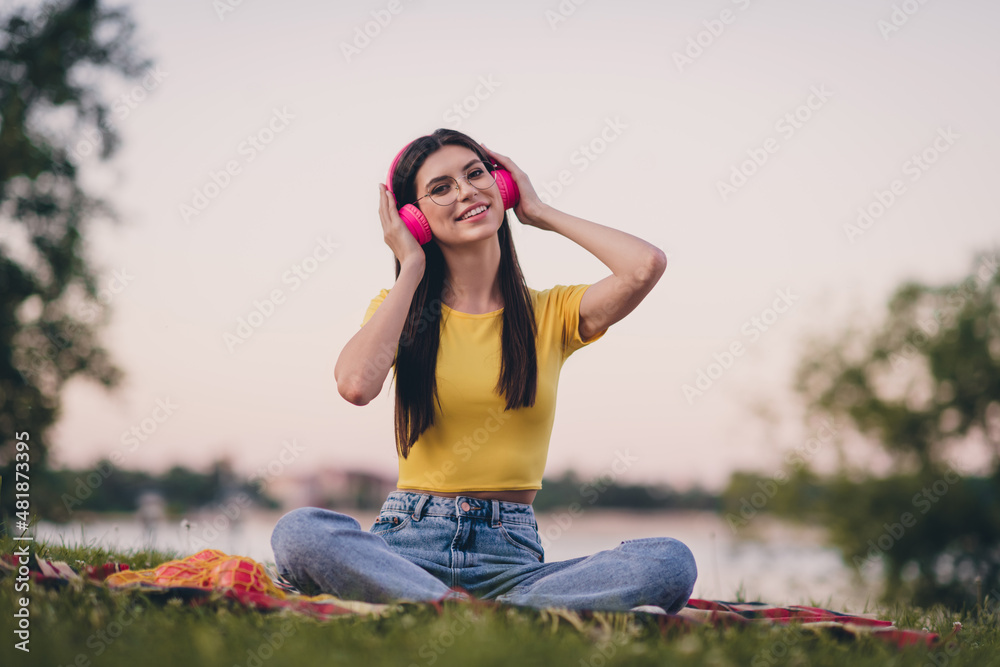 Full body photo of charming lovely lady sitting plaid blanket hands touch headphones have good mood outside Full body photo of charming lovely lady sitting plaid blanket hands touch headphones have good mood outside