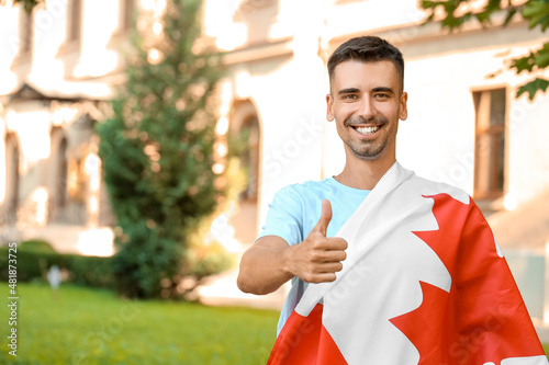 Young man with flag of Canada showing thumb-up outdoors