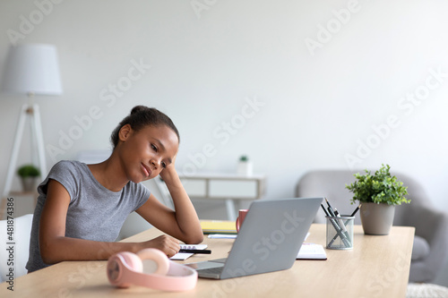 Tired young african american schoolgirl in headphones study at home with laptop, take break