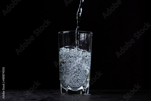 Mineral water is poured into a glass on a black background. Useful drinking mineral water.