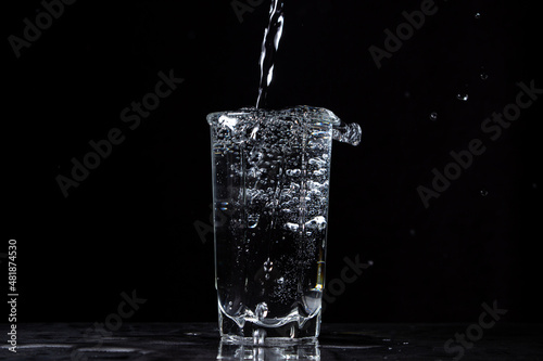 Mineral water is poured into a glass on a black background. Useful drinking mineral water.