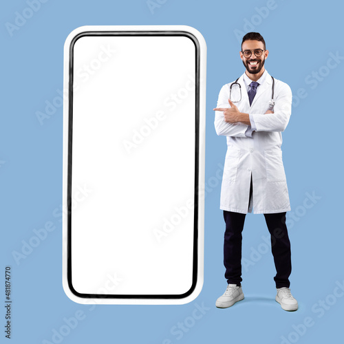 Arab Male Doctor Posing Near Big Phone Screen, Blue Background