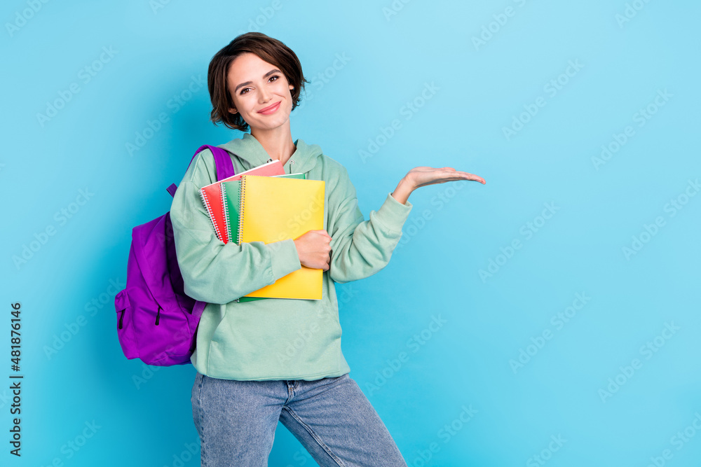 Photo of cute sweet woman wear green sweatshirt rucksack holding planners empty space isolated blue color background Photo of cute sweet woman wear green sweatshirt rucksack holding planners empty space isolated blue color background