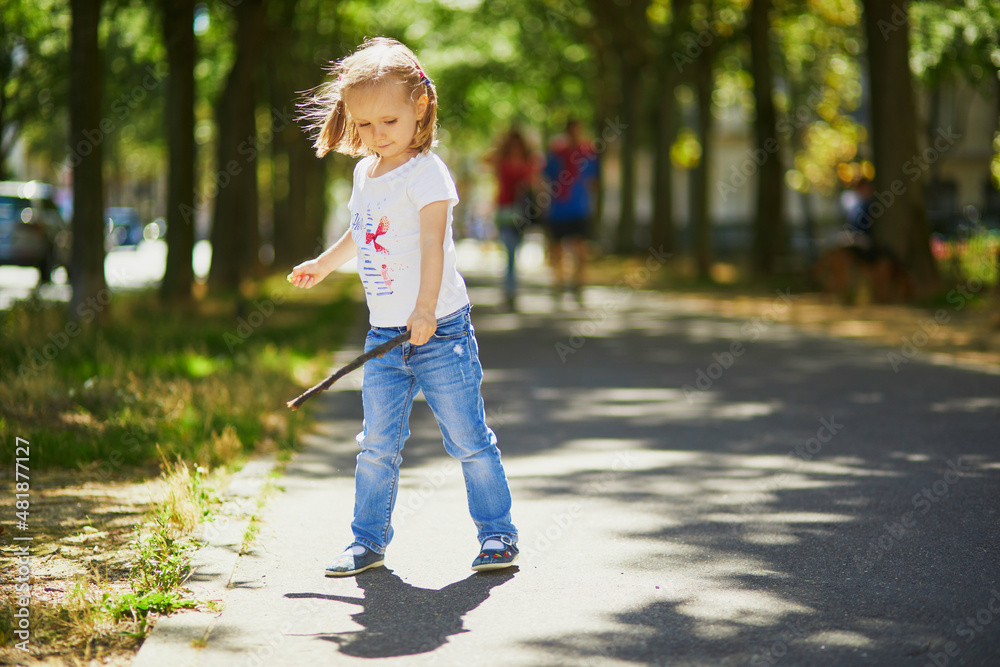 Preschooler girl playing with a stick on a sunny street. Outdoor summer activities for kids. Active games for children Preschooler girl playing with a stick on a sunny street. Outdoor summer activities for kids. Active games for children