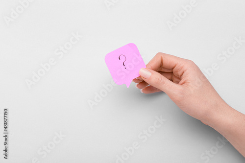 Woman holding sticky note with question mark on light background