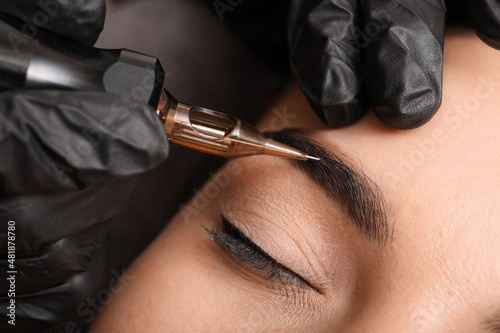 Fototapet Young woman undergoing procedure of permanent eyebrow makeup in tattoo salon, cl