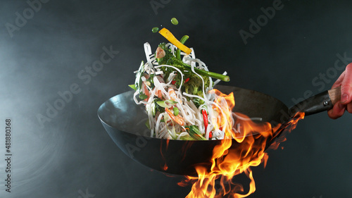 Closeup of chef throwing prawns from wok pan in fire. photo