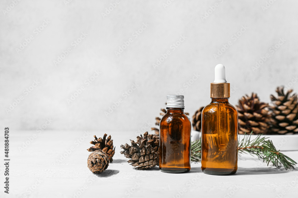 Bottles of essential oil and pine cones on light background Bottles of essential oil and pine cones on light background