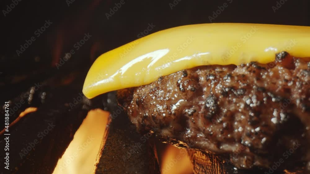 Time lapse extreme close up shot of cheese melting on top of burger meat during cooking on grill and fire