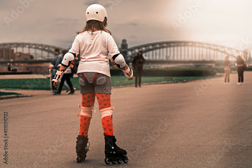Fototapeta Naklejka Na Ścianę i Meble -  A ten-year-old girl is rollerblading on the embankment. The child is wearing fall protection. Roller skating around the city.