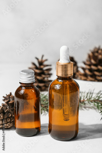 Bottles of essential oil and pine cones on light background, closeup