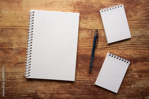trzy notatniki i długopis na drewnianym stole 