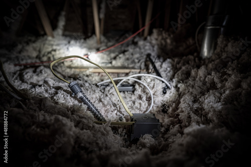 Electrical wire and conduit laying loose on blown insulation in a house attic. 