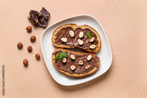 Plate of bread with chocolate paste and hazelnuts on beige background