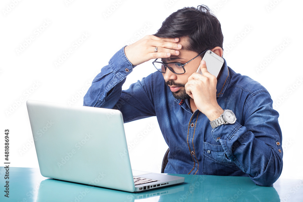 tensed man talking on cell phone and looking sadly at computer screen in isolated background tensed man talking on cell phone and looking sadly at computer screen in isolated background