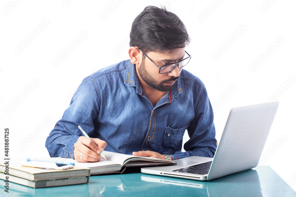 student writing on a notebook or diary while looking at laptop screen student writing on a notebook or diary while looking at laptop screen