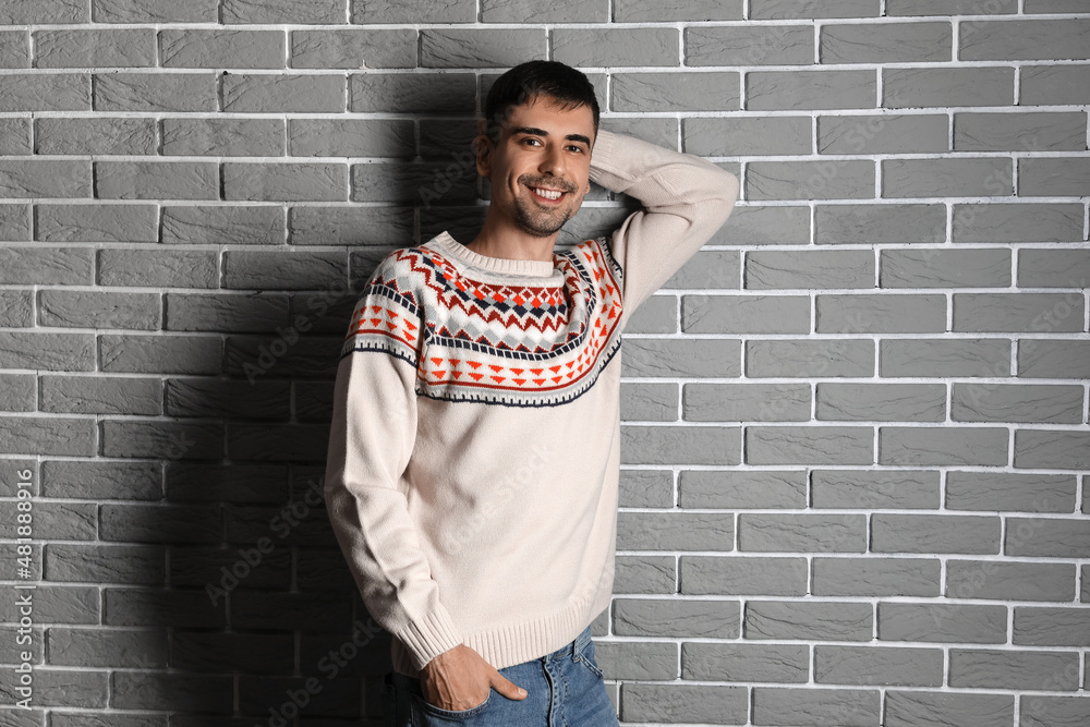 Handsome young man in knitted sweater near grey brick wall Handsome young man in knitted sweater near grey brick wall